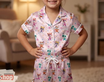 May include: Pink pajama set with a cat and star pattern. The short-sleeved top and shorts have white trim. The pajama set is made of a silky material. The child is smiling and wearing the pajama set.