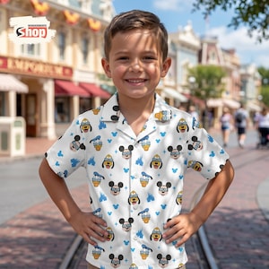 May include: A white button-down shirt featuring a repeating pattern of Mickey Mouse, Donald Duck, and Pluto wearing sunglasses. The shirt also has blue castle and Mickey head icons. The shirt is worn by a young person.