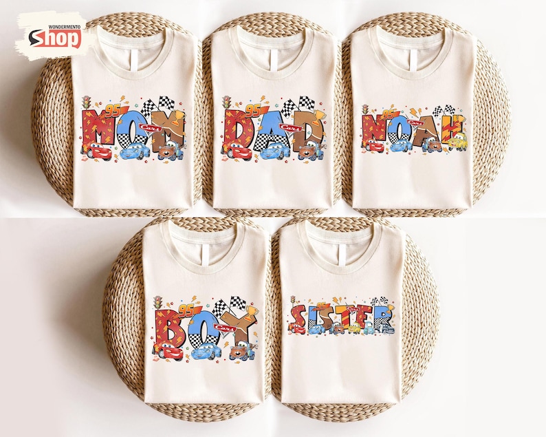 May include: Five off-white t-shirts with racing-themed designs. Each shirt features a different word: "MOM", "DAD", "NOAH", "BOY", and "SISTER", with colorful race cars and checkered flags. The text is in various colors and fonts.