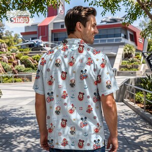 May include: A light blue short-sleeve button-down shirt featuring an all-over print of Disney characters including Mickey Mouse, Minnie Mouse, Goofy, and Spider-Man, interspersed with nautical icons like anchors, ship wheels, and life preservers.