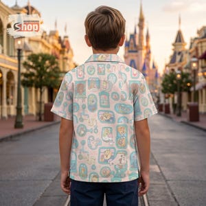 May include: A light pink button-up shirt with a repeating pattern of cartoon characters in light blue frames and piping. The shirt is short-sleeved and worn by a person facing away from the camera. The shirt has the text "Wondermento Shop" in the upper left corner.