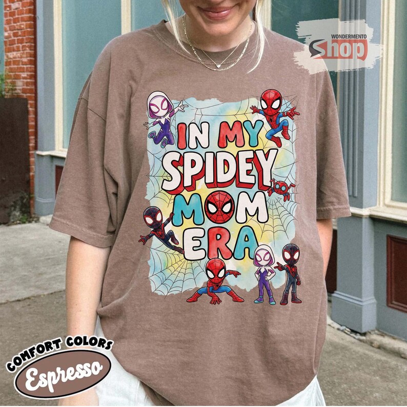 May include: Espresso-coloured t-shirt with the text "IN MY SPIDEY MOM ERA" and Spider-Man characters. The design includes a spider web background and various Spidey characters in action poses. The shirt is from Comfort Colors.