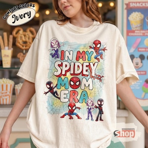 May include: Ivory-coloured t-shirt featuring the text "IN MY SPIDEY MOM ERA" and Spider-Man characters. The design includes a spider web background and the words "COMFORT COLORS" and "Ivory" in a circle.