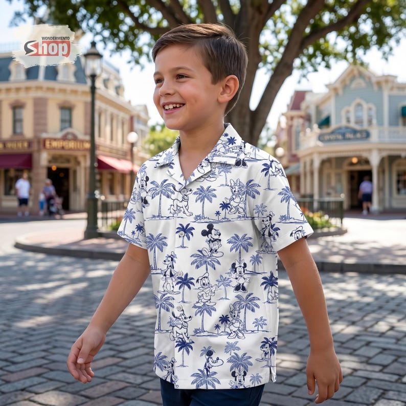 May include: A short-sleeved button-down shirt in white featuring a repeating blue pattern of Disney characters including Mickey Mouse, Minnie Mouse, Goofy, and Donald Duck interspersed with palm trees. The shirt has a classic collar and front buttons.