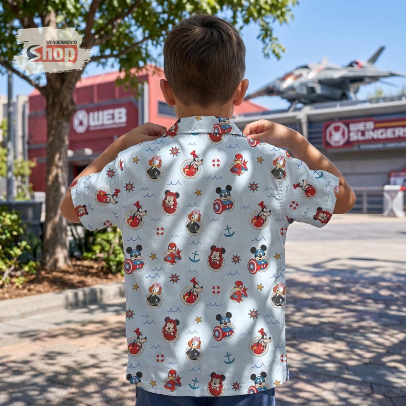 May include: A light blue short-sleeve button-down shirt featuring an all-over print of cartoon characters including Mickey Mouse, Goofy, and Spider-Man, interspersed with nautical icons like anchors, life preservers, and small blue waves.