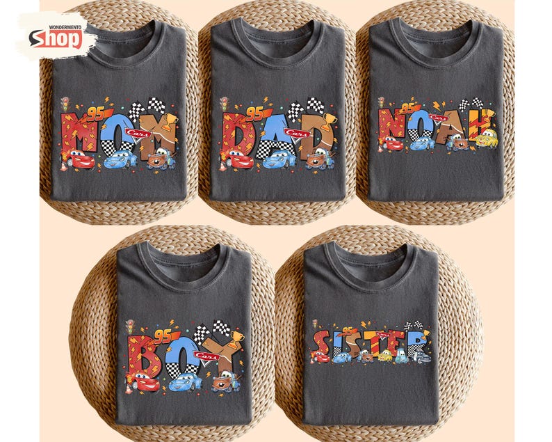 May include: Five dark gray t-shirts with colorful text and car graphics. The shirts read "MOM", "DAD", "NOAH", "BOY", and "SISTER". Each shirt features a checkered flag and the number "95".