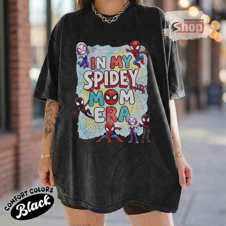 May include: Black t-shirt with the text "IN MY SPIDEY MOM ERA" in a colourful design featuring Spider-Man characters. The shirt is a Comfort Colors brand.