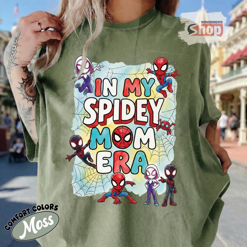 May include: A moss green t-shirt with the words "IN MY SPIDEY MOM ERA" in a colourful design. The graphic includes Spider-Man characters and a spiderweb. The shirt is from Comfort Colors.