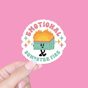 May include: A round sticker with a cartoon dumpster on fire. The dumpster has a face and is wearing a surprised expression. The text around the dumpster reads "Emotional Dumpster Fire".