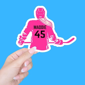 K&ouml;nnte beinhalten: Rosafarbene Silhouette eines Hockeyspielers mit dem Namen Maddie und der Nummer 45 auf der R&uuml;ckseite des Trikots.