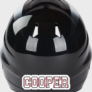 May include: Black baseball helmet with a white stripe and a red and white baseball stitch design that says "COOPER" on the back.