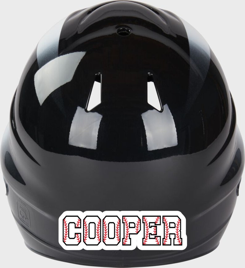 May include: Black baseball helmet with a white stripe and a red and white baseball stitch design that says "COOPER" on the back.