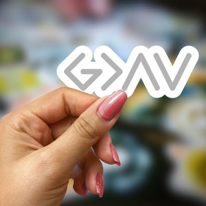 May include: A white sticker with the text "G>V" in gray lettering. The sticker is being held by a hand with pink nail polish.