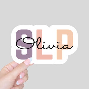 May include: A sticker with the letters "SLP" in pastel pink, purple, and orange. The letters are outlined in white. The name "Olivia" is written in black cursive script below the letters.