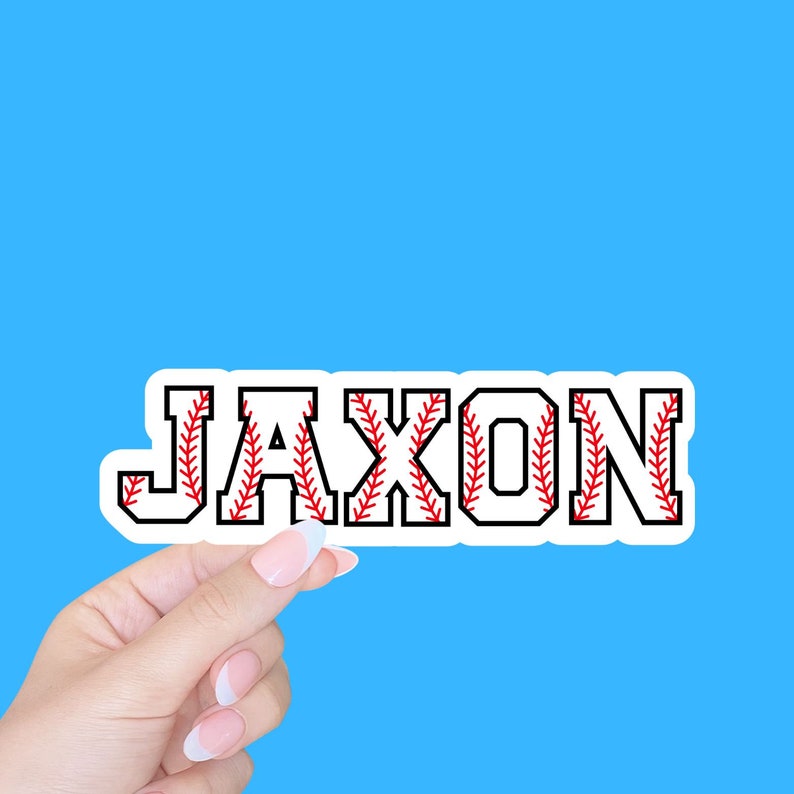 May include: A white sticker with the name "Jaxon" written in black letters. The letters are outlined with red stitching that resembles a baseball.