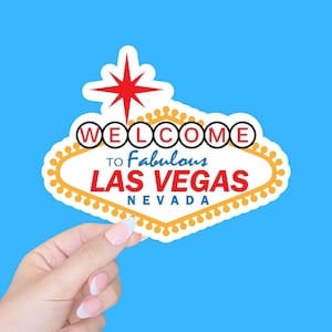 May include: A white sign with a red star and the words "Welcome to Fabulous Las Vegas Nevada" in black and yellow circles.