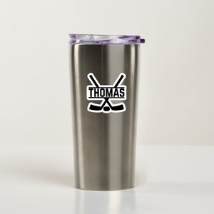May include: A stainless steel tumbler with a black and white sticker featuring crossed hockey sticks and the name "THOMAS".