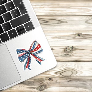 May include: A red, white, and blue bow with stars on the fabric. The bow is on a silver laptop.