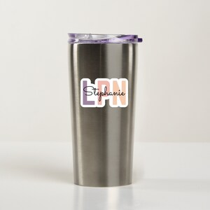 May include: A stainless steel tumbler with a purple lid and a sticker that says "LPN Stephanie" in colorful letters.