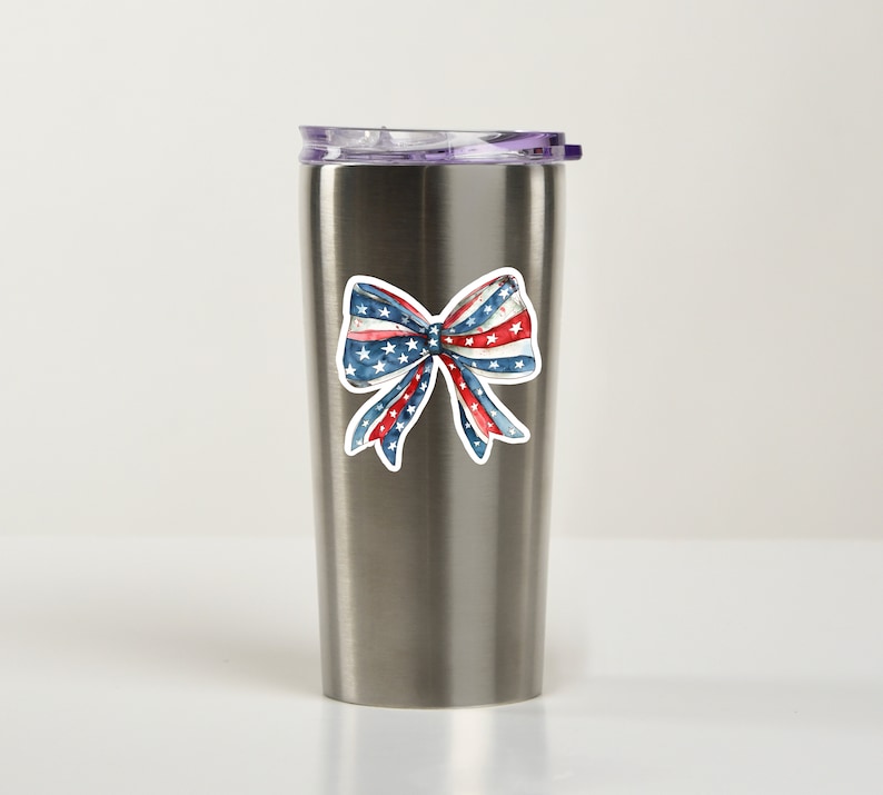 May include: A stainless steel tumbler with a red, white, and blue bow sticker. The bow is in the style of the American flag.
