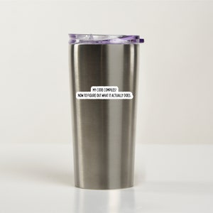 K&ouml;nnte beinhalten: Eine Edelstahl-Reisebecher mit einem lila Deckel. Der Becher hat einen Aufkleber mit der Aufschrift "Mein Code kompiliert! Jetzt muss ich herausfinden, was er eigentlich tut."