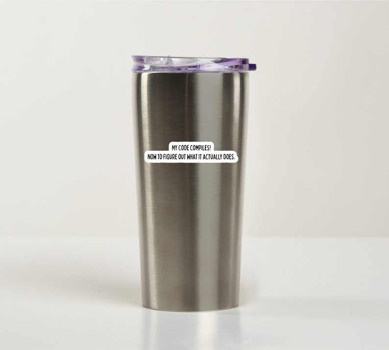 K&ouml;nnte beinhalten: Eine Edelstahl-Reisebecher mit einem lila Deckel. Der Becher hat einen Aufkleber mit der Aufschrift "Mein Code kompiliert! Jetzt muss ich herausfinden, was er eigentlich tut."