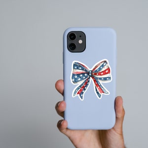 May include: A blue phone case with a white outline of a red, white, and blue bow with stars.