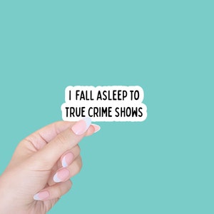 May include: A white sticker with black text that reads "I fall asleep to true crime shows". A hand is holding the sticker in front of a turquoise background.