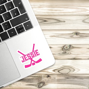 May include: Pink hockey stick decal with the name "JESSIE" on a laptop.