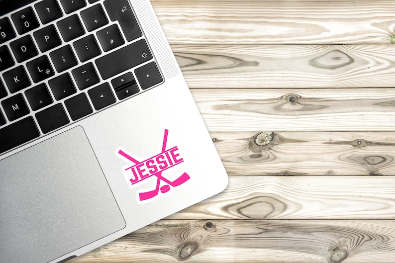 May include: Pink hockey stick decal with the name "JESSIE" on a laptop.