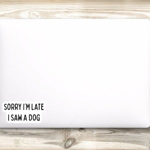 May include: White laptop with a black and white sticker that says "Sorry I'm late I saw a dog" on a wood background.