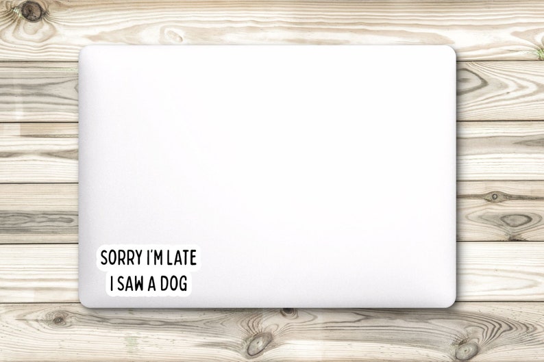 May include: White laptop with a black and white sticker that says "Sorry I'm late I saw a dog" on a wood background.