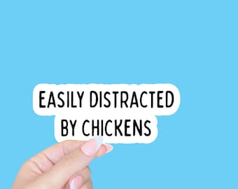 May include: A white sticker with black text that reads "Easily Distracted by Chickens" held by a hand with light pink nail polish.