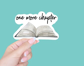 May include: A white sticker with the text "one more chapter" in black script. An illustration of an open book with white pages is below the text.