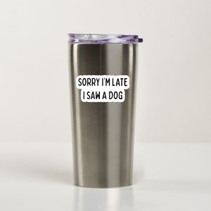 May include: A stainless steel travel mug with a purple lid and a white sticker that says "Sorry I'm late I saw a dog".