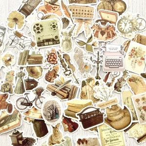 Op de afbeelding: Een set vintage stickers met verschillende illustraties, waaronder een typemachine, een fiets, een globe, een boek, een konijn, een vogel, een bloem, een klok, een koffer, een mand, een muziekinstrument en een kompas. De stickers zijn gedrukt op wit papier met een cr&egrave;mekleurige achtergrond.