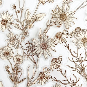 May include: A sheet of clear, transparent stickers with gold foil designs of various flowers and leaves. The stickers are perfect for adding a touch of elegance to journals, planners, and other craft projects.