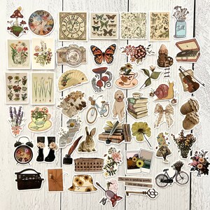 May include: A collection of vintage-style stickers featuring various designs, including flowers, butterflies, mushrooms, clocks, a snail, a rabbit, a basket, a book stack, a jar, a musical instrument, a teacup, a clock, a bicycle, and a quote about the rain. The stickers are on a white wooden background.