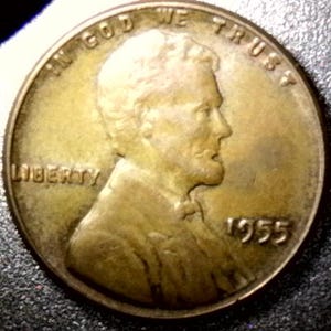 May include: A copper-colored 1955 Lincoln penny. The obverse features a profile of Abraham Lincoln, the word "LIBERTY", and the inscription "IN GOD WE TRUST". The year "1955" is visible.