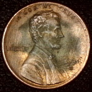May include: A close-up of a United States penny from 1984. The coin features a profile of Abraham Lincoln, with the words "LIBERTY" and "IN GOD WE TRUST" visible. The year "1984" and the mint mark "D" are also present.