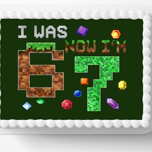 May include: A rectangular cake with white frosting trim and a dark green top. The top features pixelated text that reads "I WAS 6, NOW I'M 7" with colorful pixelated gems and accents. A fun birthday cake.