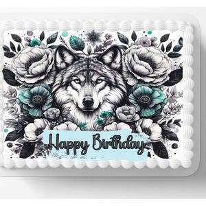 May include: A white cake with a wolf and floral design edible image. The image features a wolf's head with a black and white design, surrounded by teal and white flowers. The text "Happy Birthday" is printed in black on a light blue banner.