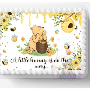 May include: A rectangular cake with a Winnie the Pooh theme. The cake features a cartoon illustration of Winnie the Pooh, honey, bees, and sunflowers. The text "A little hunny is on the way" is also included.