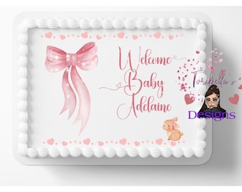 May include: A rectangular sheet cake with white frosting borders, featuring a pink watercolor bow, a small bunny, and the text Welcome Baby Adelaine in pink script. The design includes small pink hearts along the top and bottom edges.