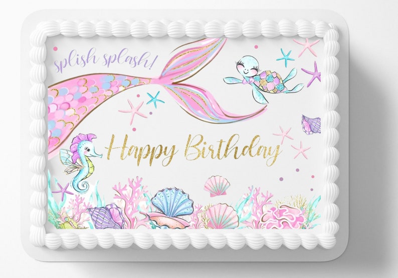 May include: A rectangular cake with white icing, decorated with a mermaid theme. The cake features a mermaid tail, seahorse, turtle, and the words "Happy Birthday" in gold. Seashells and coral complete the design.