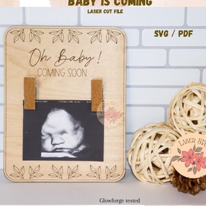 Puede incluir: Un letrero de madera con el texto "Oh Baby! Coming Soon..." y dos pinzas para sujetar una foto. El letrero está decorado con hojas y tiene un acabado de madera clara.