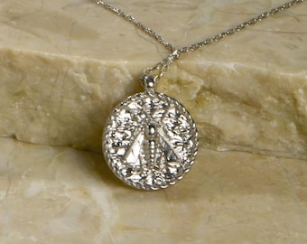 Peut inclure: Un collier en chaîne argent avec un pendentif rond orné d'un motif complexe. Le pendentif a une surface texturée en relief.