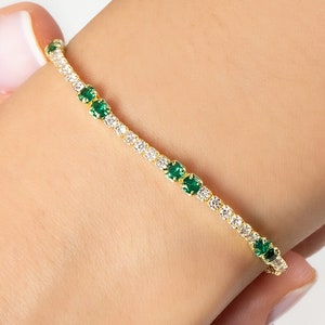 May include: A gold bracelet with a row of small green and white stones.