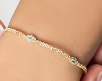 May include: A gold bracelet with three evil eye charms. Each charm is surrounded by small clear stones and has a blue center.