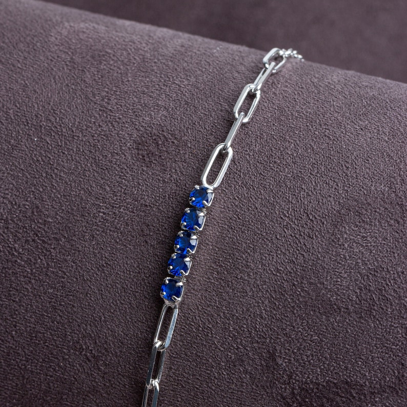 May include: A silver chain bracelet with a row of blue gemstones.